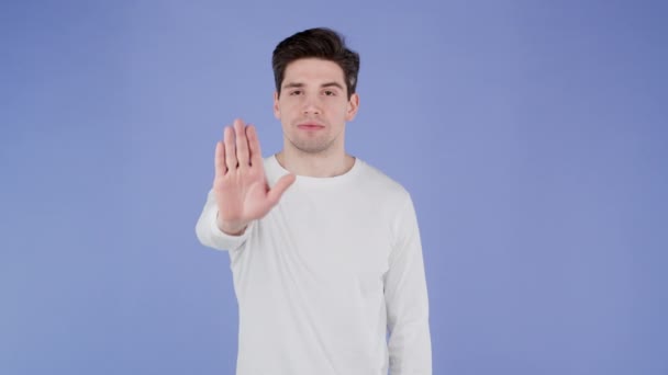 Portrait of serious man showing rejecting gesture by stop palm hand sign. Guy isolated on violet background. — Stock Video