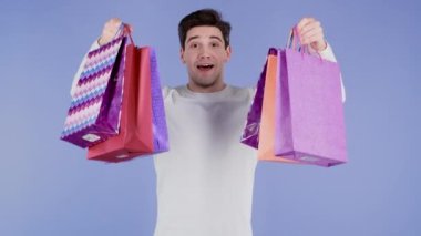 Yakışıklı adam menekşe stüdyosunun arka planında alışveriş poşetleri tutuyor. Adam indirimli satışlardan hediyeler aldı..