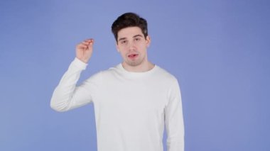 Yakışıklı, sıkılmış bir adam, elleri ve mor arka planda izole edilmiş yuvarlanan gözlerle jest yapıyor. Boş vaatler, falan filan. Yalancı.