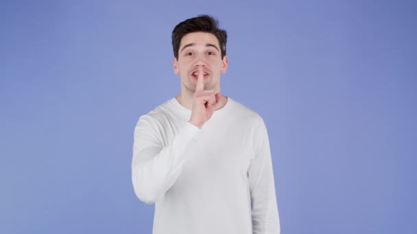 Usmívající se muž drží prst na rtech přes fialové pozadí. Gesto shhh, tajemství, ticho. — Stock video