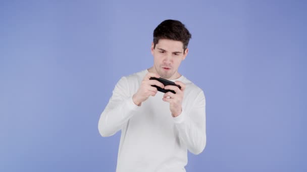 Красивий чоловік грає в гру на смартфоні на фіолетовій стіні студії. Використання сучасних технологій - додатків, соціальних мереж . — стокове відео