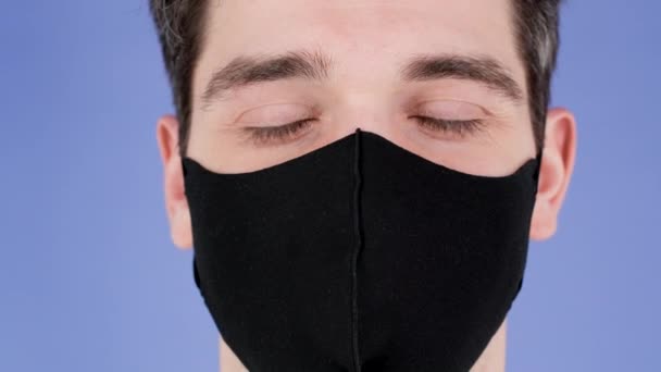 Nöjd man tog bort skyddande svart ansiktsmask som symbol för pandemisk, epidemisk slut. Lila studio bakgrund. Covid-19, coronavirus, vaccinationskoncept. — Stockvideo