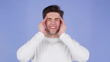 Baş ağrısı çeken genç bir adam, stüdyo portresi. Adam ellerini başının üstüne koyuyor, menekşe arka planda izole edilmiş. Sorunlar, ilaç, hastalık kavramı