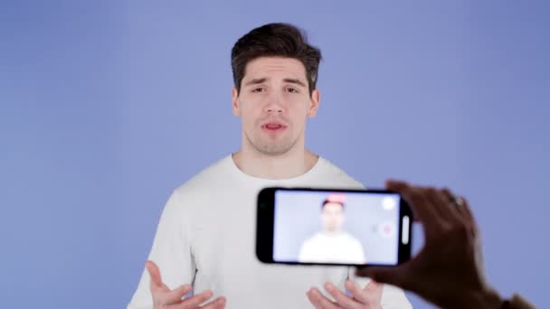 笑顔ブロガーの男は、紫の背景に彼のスマートフォンでオンライン新しいビデオブログ、 vlogを作成します。会議中にカメラに向かって話すインフルエンサーの通話記録. — ストック動画
