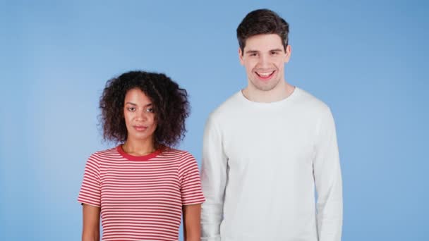 Mujer africana alegre y hombre blanco mostrando sí signo, asiente con la cabeza aprobadamente. Pareja interracial sonriente positiva, emociones, concepto de lenguaje corporal. Fondo estudio azul. — Vídeos de Stock