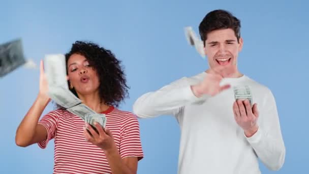 Opgewonden interraciale paar verspreidt contant geld - USD valuta dollars bankbiljetten op de blauwe muur. Symbool van succes, winst, overwinning. Afrikaanse vrouw en blanke man is flush, te veel geld uitgeven — Stockvideo