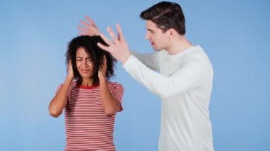 Genç beyaz adam duygusal olarak mavi arka planda karısına ya da kız arkadaşına bağırıyor. Sıkılmış Afrikalı kadın elleriyle kulaklarını kapatıyor. Çatışma kavramı, ilişkilerde sorunlar, ırklar arası çiftler.