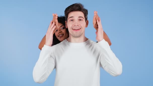 Mulher afro-americana fecha os olhos de seu amado namorado antes de surpreendê-lo. casal interracial em fundo estúdio azul. Amor, férias, conceito de felicidade. — Vídeo de Stock