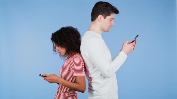 Міжрасова пара стоїть спиною одне до одного і друкує повідомлення або серфінг Інтернету з мобільних телефонів. Технології, відстані, смартфони, соціальні мережі — стокове відео