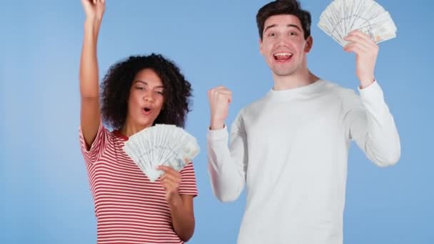 Sorprendido feliz pareja interracial emocionado mostrando dinero USD billetes en dólares en la pared azul. Símbolo de éxito, ganancia, victoria. Mujer africana y hombre blanco ganan la lotería. — Vídeos de Stock