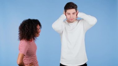 Genç Afrikalı bir kadın mavi arka planda kocasına ya da erkek arkadaşına duygusal olarak bağırıyor. Sıkılmış adam kulaklarını elleriyle kapatır. Çatışma kavramı, ilişkilerde sorunlar, ırklar arası çiftler.