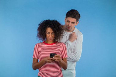 Yakışıklı adam Afrikalı kız arkadaşının omzundan bakıyor, cep telefonuyla iletişim kuruyor. Kıskançlık ve ihanetle şok olan adam. Mavi özgeçmiş.