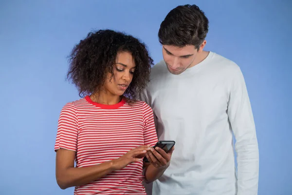 Mobil cihaz kullanan ırklar arası genç bir çift. Afrikalı kadın uygulamalardan bahsediyor ve erkeklere uygulamanın nasıl kullanılacağını anlatıyor. Mavi stüdyo arka planı — Stok fotoğraf