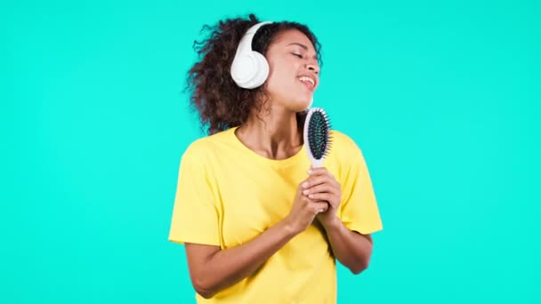 Африканская женщина поет и танцует с расчёской или расчёской вместо микрофона на фоне чирликовой студии. Подросток в наушниках веселится, слушает музыку, мечтает стать знаменитостью. — стоковое видео