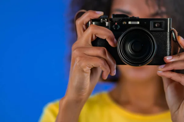 Молода американка-афроамериканка фотографується з камерою DSLR на синьому фоні в студії. Дівчинка посміхається, як фотограф.. — стокове фото