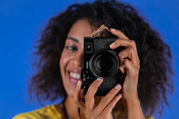 ウクライナのオデッサ- 2021年6月。アフリカの女性は、デジタル一眼レフカメラで写真を撮る-スタジオで青の背景に富士フイルムX100f 。写真家として笑う少女. — ストック写真
