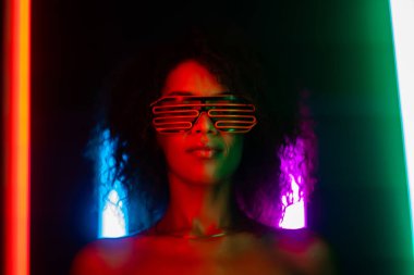 Siber punk tarzı, göz kamaştırıcı Afrikalı bir kadının renkli bir ışık altında partideki portresi. Gece kulübü, fütüristik kostüm ve neon gözlükler. Gençlik, Zoomer Z jenerasyonu.