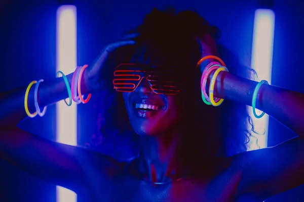 Retrato de estilo cyberpunk de la glamorosa mujer africana en la fiesta bajo una luz brillante y colorida. Discoteca, disfraz futurista y gafas de neón. Adolescente, zoómero Z-generación. —  Fotos de Stock