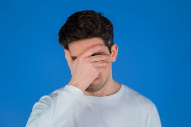 Genç adam facepalm hareketi yapıyor, hayır, unuttum. Mutsuz adam üzüntü, pişmanlık, drama, başarısızlık hissediyor. Mavi duvarda izole edilmiş.