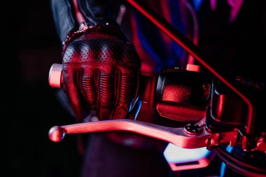 Deri eldiven giyen motosikletli el renkli şehir ışıklarında ivmeölçer kolu büker. Motosiklet gidonu boyunca hareket eden bir kamera. Gece hayatı ve motorcu kültürü kavramı.