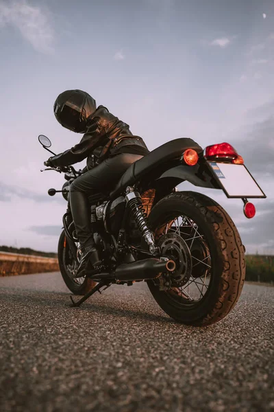 Elegante mujer motociclista en casco y chaqueta de cuero sentado en motocicleta vintage. Conductora al aire libre sobre fondo natural. Viaje, corredores de café, velocidad, concepto de libertad. —  Fotos de Stock
