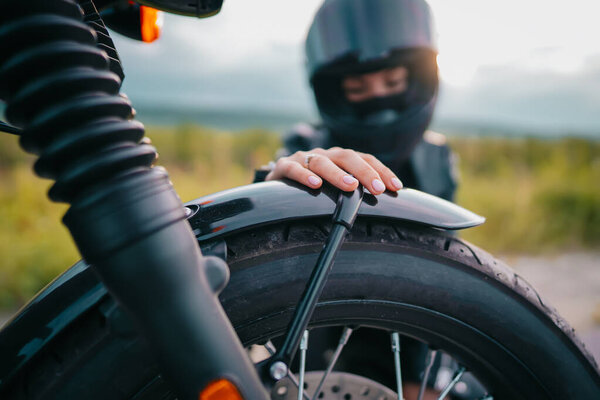 Portrait of confident motorcyclist woman in helmet sitting near bike. Young driver biker outdoors at sunset.