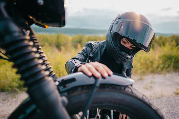 Portrait of confident motorcyclist woman in helmet sitting near bike. Young driver biker outdoors at sunset.