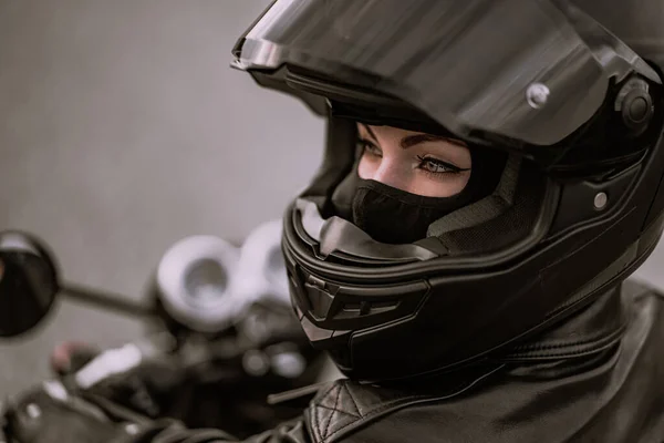 Siyah motosiklet üzerinde oturan kask ve deri ceketli şık motosikletli kadın. Kadın sürücü, doğa arka planında. Trip, cafe yarışçıları, hız, özgürlük konsepti. — Stok fotoğraf