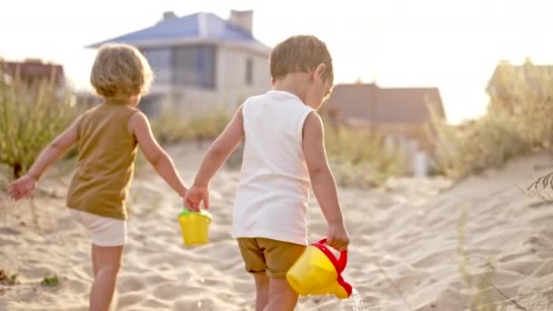 Söta små pojkar bröder går på sandstrand med burkar. Sommaren solig dag. Småbarn tvillingar med färgglada krukor. Naturestetiska barn på naturen bakgrund. — Stockvideo