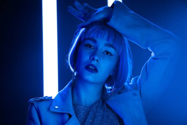 Kısa saçlı karizmatik kadın kurşun mavisi neon lambaların yanında poz veriyor. Hippi modacı kız. Modern model pop kıyafeti, etkileyici yaşam tarzı..