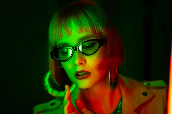 Charming woman with dyed green hair posing under neon light. Unusual mysterious lady in sunglasses, nightlife concept. Modern model pop outfit, influencer lifestyle. — Stock Photo, Image