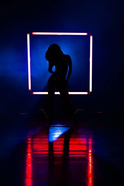 赤いランプの背景の輝く広場で踊る女性のシルエット。彼女は魅惑的に見えます.セクシーな服-ヒール。ブルースモーキースタジオ. — ストック写真