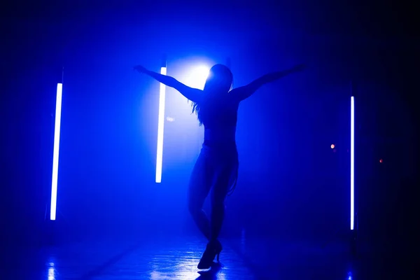 Frau im sexy Outfit mit Absätzen tanzt sinnlich im dunklen Studio mit blauen Lampen. Kreative Dame, die sich aktiv zur Musik bewegt. Konzept aus Choreographie, Tanz, Performance. — Stockfoto