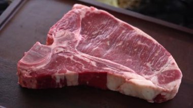 Rotating T-bone steak - raw marble beef fillet. Delicious juicy meat close-up view. Presentation of dish in luxury restaurant.