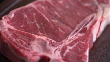 Super close-up of T-bone steak - raw marble beef fillet, aged prime rare delicious juicy meat. Side view. Presentation of dish in luxury restaurant ready for bbq.