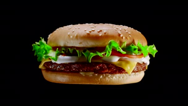 Rotating flying appetizing burger with meat cutlet, onion, vegetables, melted cheese, lettuce and mayonnaise sauce. Isolated hamburger spinning around on black background, close-up view — Αρχείο Βίντεο