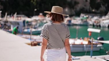 Yatları olan bir liman. Çizgili tişörtlü ve hasır şapkalı genç bir kadın güney Avrupa kıyılarında yürüyor. Lüks tatil, seyahat, rahatlatıcı konsept.