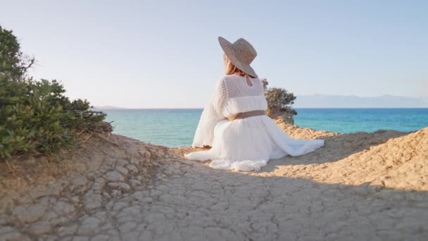 Boho mulher turística sentada no penhasco sobre mar Mediterrâneo Canal DAmour, arrepiante. Senhora de vestido e chapéu de palha desfrutando de férias de verão em Corfu, Grécia. Natureza selvagem fundo. — Vídeo de Stock
