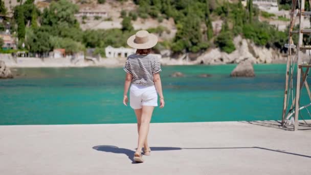 Främmande turist kvinna promenader i piren på Paleokastritsa byn, lyx resort Korfu. Fantastisk turkos havsvatten bakgrund. Flicka utforska resmål, njuta av semester. — Stockvideo