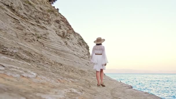 Femme élégante en robe blanche aérée marchant sur la plage d'argile près de la mer Méditerranée. Dame appréciant explorer la nature sauvage, vacances d'été en Grèce.