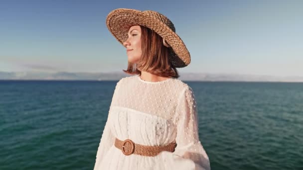 Πορτρέτο της κομψής γυναίκας σε λευκό φόρεμα ποζάρουν στην παραλία γκρεμό κοντά στη Μεσόγειο θάλασσα. Κυρία που απολαμβάνει τη φύση, καλοκαιρινές διακοπές στην Ελλάδα. Boho νυφικό, εμφάνιση νύφης. — Αρχείο Βίντεο