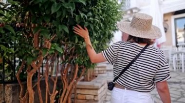 Hasır şapkalı, Yunanistan ya da İtalya 'daki antik kenti keşfeden gezgin kadının arka planı. Kadın yerel Akdeniz mimarisini geziyor. O, yazın şehirde dolaşırken iyi vakit geçiriyor.