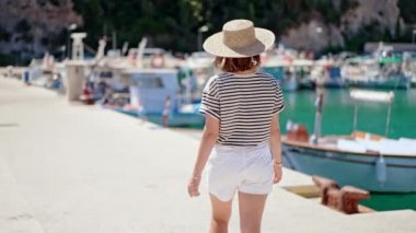 Yatları olan bir liman. Güney Avrupa kıyıları boyunca çizgili tişört ve hasır şapkalı tanınmayan genç bir kadın yürüyor. Lüks tatil, seyahat, rahatlatıcı konsept.