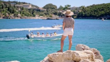 Çizgili seyahat kıyafeti giymiş bir kadın motorlu teknelerde seyrediyor. Hasır şapkalı kadın ranzada duruyor. Mavi deniz arka planı. Riviera Sahili, lüks tatil konsepti.
