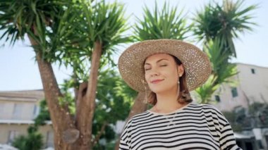 Hasır şapkalı hoş bir kadının portresi palmiye ağaçlarında samimi bir şekilde gülümsüyor. Yunan tatil köyünde tatil yapan bir kız. Popüler adayı ziyaret eden kadın, seyahat yaşam tarzı konsepti.