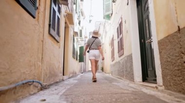 Yunanistan adasındaki eski Avrupa kenti dar sokaklarını tek başına gezen turist kadınların arka manzarası. Bayan gezici yerel mimari. O, yazın şehirde dolaşırken iyi vakit geçiriyor.
