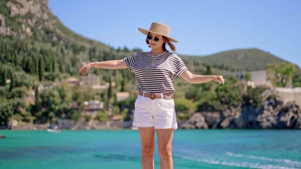 Jovem mulher despreocupada feliz em chapéu de palha em pé sobre fundo azul-turquesa baía do mar e desfrutar de férias. Menina imaginar que ela é pássaro. Destino de viagem, natureza incrível, sul da Europa. — Vídeo de Stock