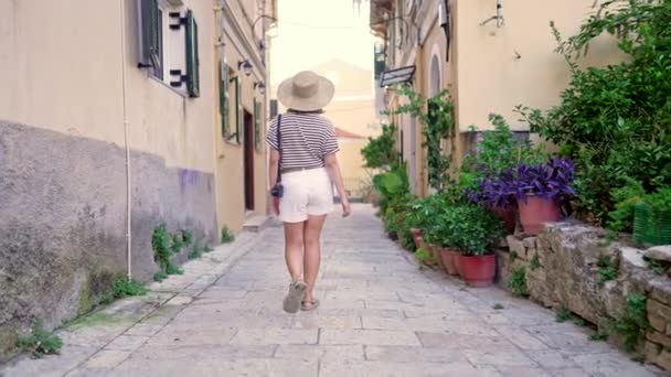 Donna turistica in cappello di paglia che cammina su strette strade antiche. Ragazza che trascorre le vacanze in Grecia. Lady visite architettoniche locali. Si sta divertendo a girovagare per la città in estate. — Video Stock