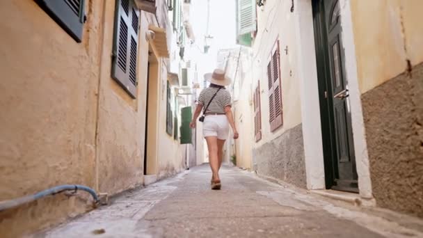 Vista posteriore della donna turistica che cammina da sola, esplorando le vecchie strade strette della città europea sull'isola di Grecia. Lady visite architettoniche locali. Si sta divertendo a girovagare per la città in estate. — Video Stock