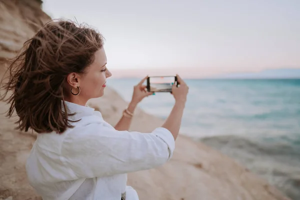 Fiatal nő videózik mobiltelefonnal a tengerparton, közel a kék tengerhez. Lány okostelefon, fotózás a szociális alkalmazás, élvezi a nyaralás ideje. — Stock Fotó
